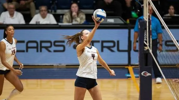 San Diego volleyball player reaching one hand toward a ball near the net