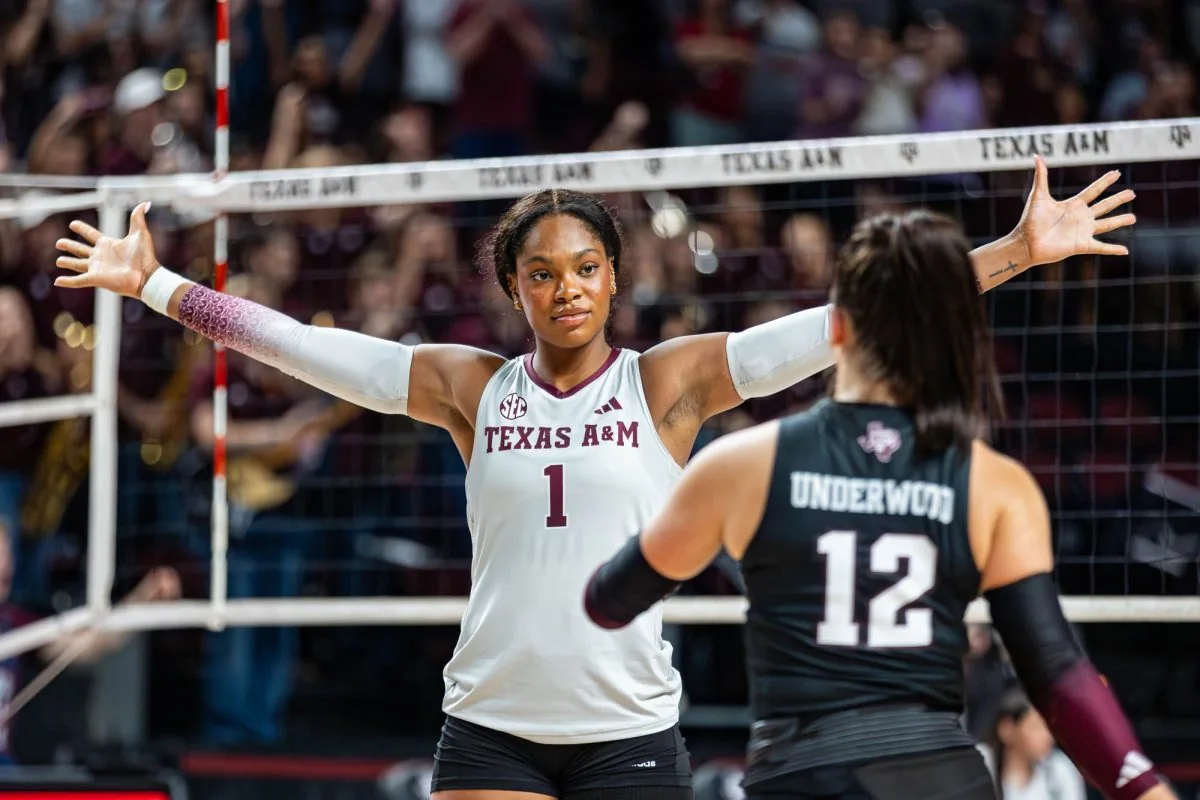 Texas A&M volleyball player in a white jersey spreading her arms near the net