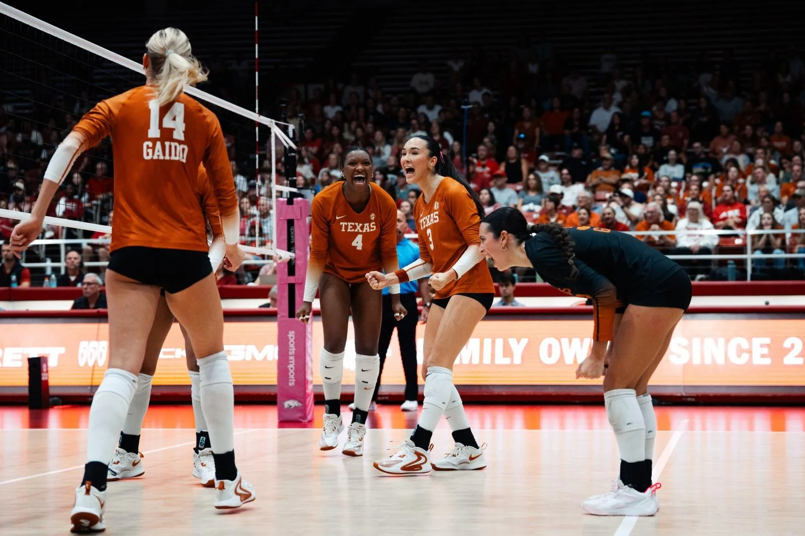 Texas volleyball players in orange celebrating in front of spectators at an away court