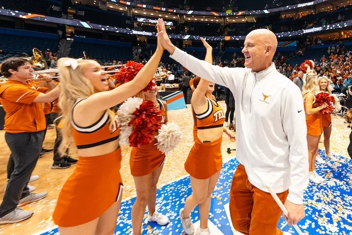 Texas volleyball coach high-fiving a cheerleader on a court covered in confetti