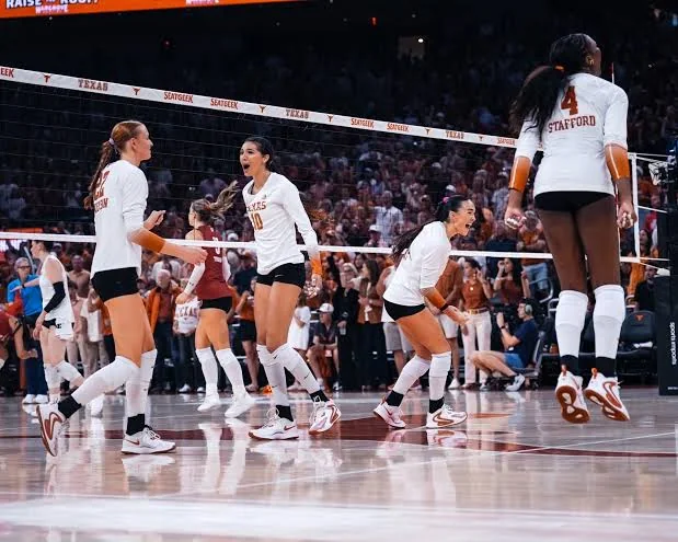Texas volleyball players celebrating together on an indoor court