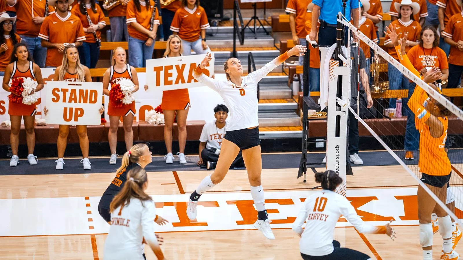 Texas volleyball player in a white jersey attacking beside the net with fans behind the court