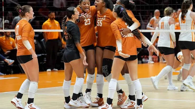 Texas volleyball teammates in orange gathering after a point with opponents across the net