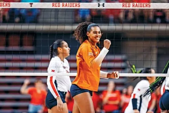 Texas volleyball player in orange celebrating beside a net marked Red Raiders