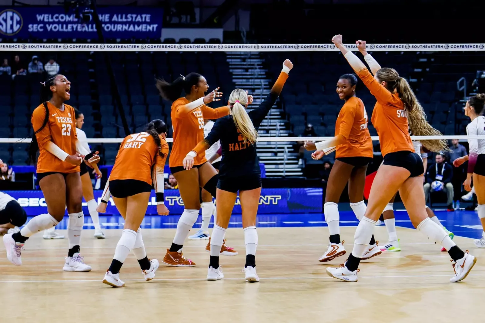 Texas volleyball players in orange celebrating beneath SEC tournament signage