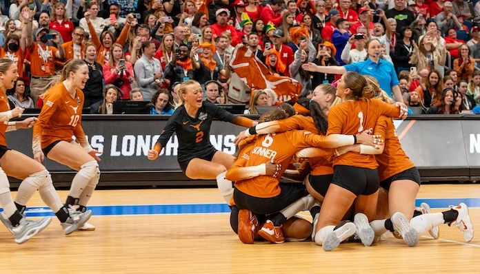 Texas volleyball players in orange jerseys celebrating in a group on the floor