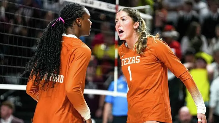 Two Texas volleyball players in orange jerseys communicating beside the net