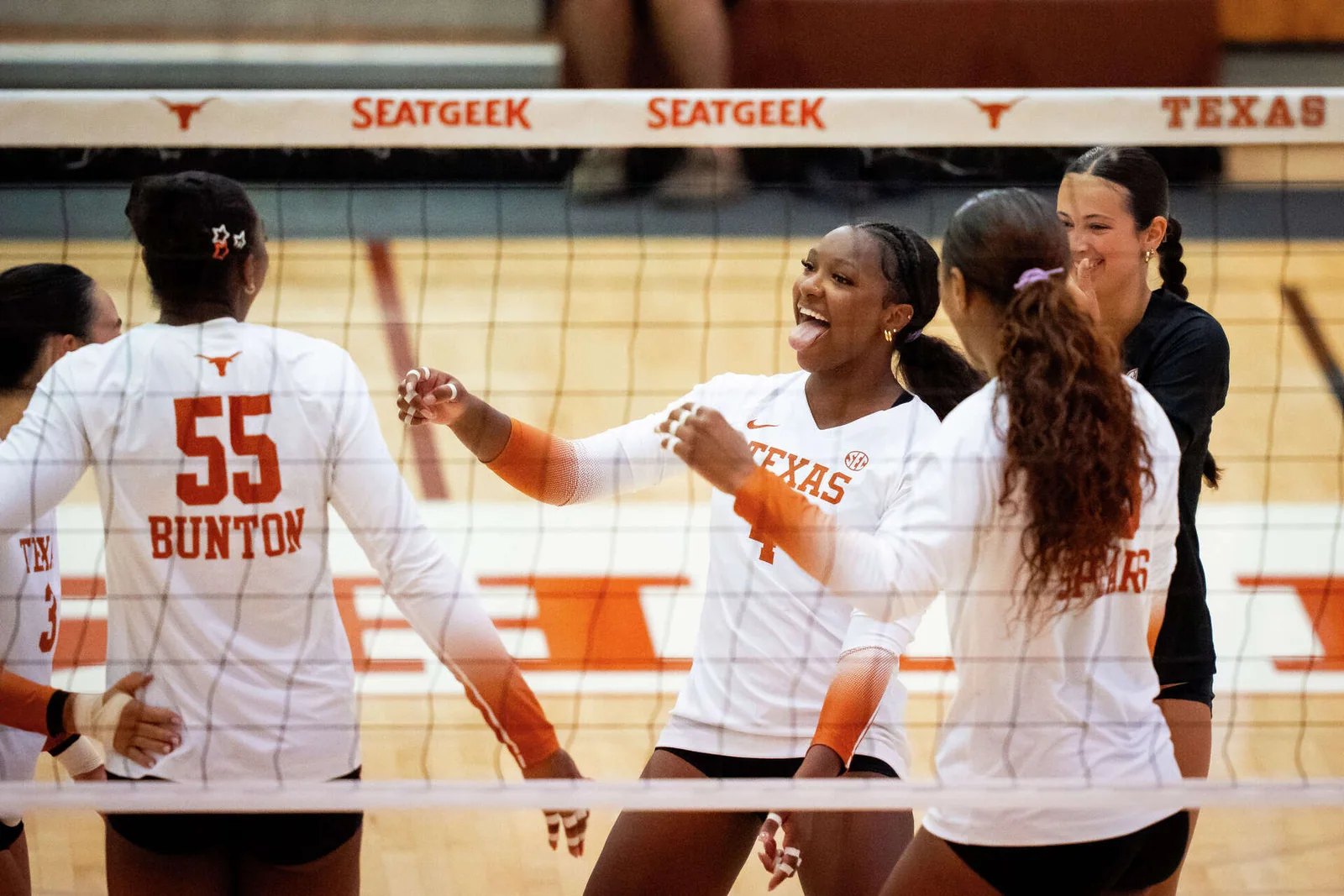 Texas volleyball teammates in white jerseys smiling together at the net