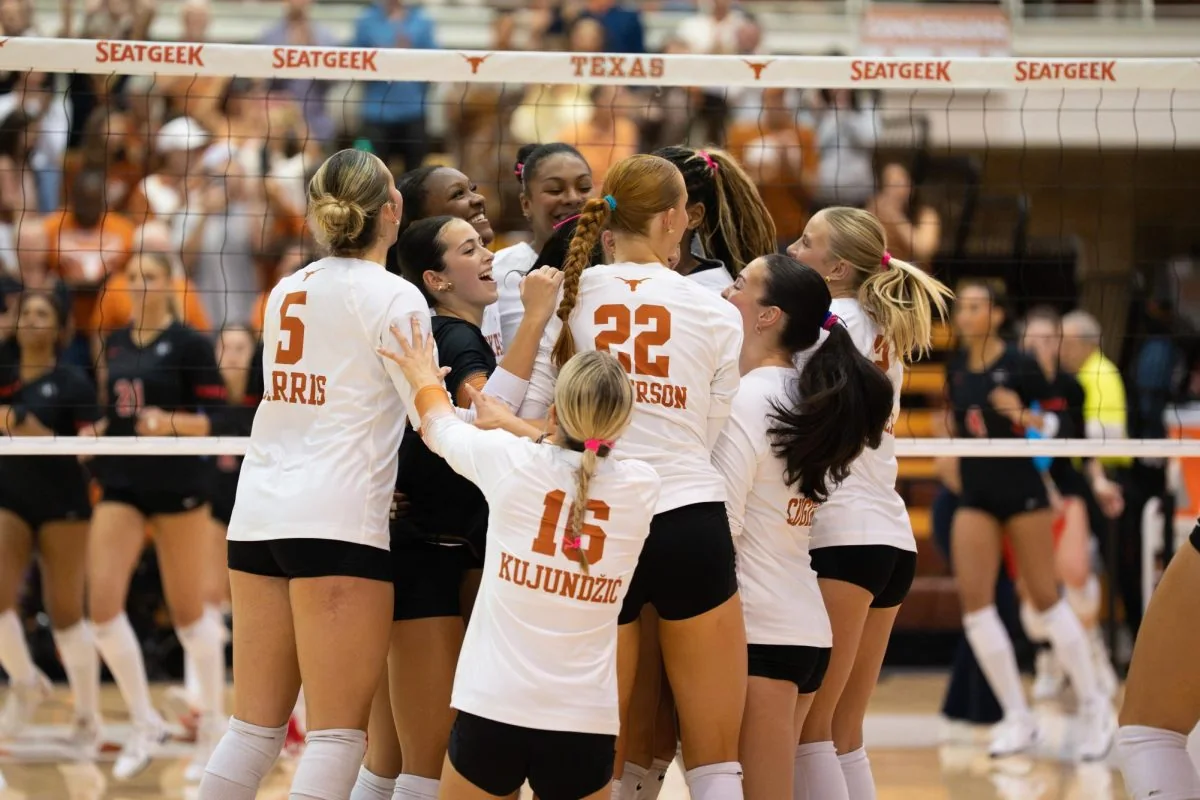 Texas volleyball players in white jerseys huddling near the net